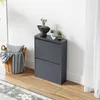 A dark gray shoe cabinet with two flip-down doors, decorated with small potted plants on top, stands against a white wall next to a woven basket filled with a pillow and striped blankets. Produktbild-Vorschau