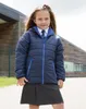 A young girl wearing a school uniform and a navy blue padded jacket stands outside a school building. Produktbild-Vorschau