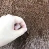 A hand is shown pinching a brown shaggy rug. Náhled obrázku produktu
