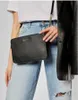 A person wearing jeans and a white t-shirt, holding a black Michael Kors crossbody bag. Podgląd zdjęcia produktu