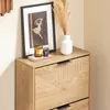A close-up view of a wooden shoe cabinet with decorative grooves on the drawers, featuring a framed picture and decorative items on top. Podgląd zdjęcia produktu