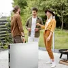 Three people are standing around a folded table in an outdoor setting, possibly a backyard or park. Produktbild-Vorschau