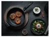 A frying pan with three cooked patties sits on a wooden board, next to a plate with a patty on a bed of greens, and a bowl of dip. Produktbild-Vorschau