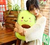 A woman is hugging a plush avocado toy in a room with wooden furniture and plants. Produktbild-Vorschau