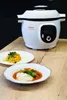 A white Tefal Cook4me+ smart multi-cooker is displayed on a wooden table, with two plates of food in front of it. Podgląd zdjęcia produktu
