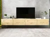 A modern, floating media console with a light wood finish is mounted on a gray concrete wall, with a black television displayed on top. Several small decorative items are placed on the console, including potted plants and books. Produktbild-Vorschau