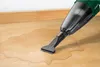 A handheld vacuum cleaner is being used to clean up a spill of liquid on a wooden floor. Produktbild-Vorschau