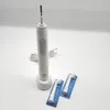 A white electric toothbrush with its charging base and two replacement brush heads in packaging, set against a plain background. Produktbild-Vorschau