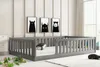 A child's bed with a grey wooden frame and a white mattress, decorated with black and white monster-themed artwork on the wall and whale-shaped plush toys on the bed and floor. Produktbild-Vorschau