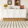 A modern white sideboard with arched doors and a fluted wood base, decorated with sunflowers and a vintage record player on top, placed in a well-lit room with a patterned rug in the foreground. Náhľad obrázku produktu