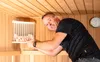 A man is in a sauna, pointing to a light fixture with stones. Produktbild-Vorschau