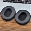 Two black ear pads are placed on a wooden surface in front of a laptop keyboard. Voir les images du produit