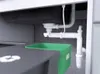 Underneath a sink, showing plumbing and a trash bin. Náhled obrázku produktu