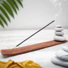 An incense stick burning on a wooden holder, with stacked stones and a palm leaf in the background. Podgląd zdjęcia produktu