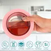 A hand holding a pink, round food container filled with a brown liquid, with icons and text describing its features at the bottom. Produktbild-Vorschau