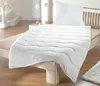 A neatly made bed with a white duvet and pillow, set in a bright, minimalist bedroom.