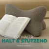A taupe-colored reading pillow is placed behind an open book on a wooden surface. Produktbild-Vorschau