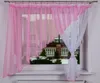 A window with pink and white sheer curtains, showing a snowy garden scene outside.