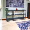 A black console table with three shelves against a light gray wall, decorated with a red vase, a plant, and a decorative bird figurine. A blue rug is on the wooden floor in front of the table. Produktbild-Vorschau