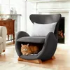 A cat is resting in a unique armchair designed with a built-in cat bed, in a living room setting with a fireplace in the background. Náhled obrázku produktu