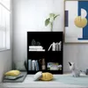 A black bookshelf in a room with a window, pillows, and a rug. Náhled obrázku produktu