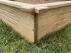 A close-up view of the corner of a wooden raised garden bed, resting on grass. Produktbild-Vorschau