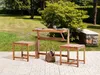 A wooden table and two stools set up on a patio in a garden setting. Produktbild-Vorschau