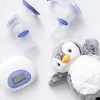 A flat lay of baby feeding items including two Lansinoh breast pumps, a white electronic pump base, and a plush penguin toy, arranged on a white background. Produktbild-Vorschau