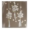 Three white crocheted snowflakes with gold beads and white tassels hanging against a blurred background of lights. Náhľad obrázku produktu
