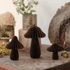 Three decorative paper mushrooms are arranged on a wooden surface, with blurred floral arrangements and a rustic wooden circle in the background. Produktbild-Vorschau