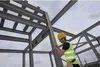 A construction worker is measuring a steel beam on a construction site. Voir les images du produit