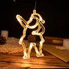 A close-up of a hanging LED Christmas decoration shaped like a reindeer, illuminated with warm yellow lights, set against a dark background with some blurred elements of a festive scene. Produktbild-Vorschau
