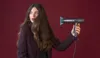 A woman holds a hairdryer against a red background. Náhled obrázku produktu
