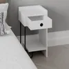 A white nightstand with one drawer partially open, next to a bed. Produktbild-Vorschau