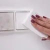 A hand with dark pink nail polish is cleaning a dirty light switch with a white sponge. Produktbild-Vorschau
