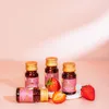 Four small bottles of liquid, likely a supplement, are arranged on a pink surface with strawberries. One bottle is lying on its side. Produktbild-Vorschau