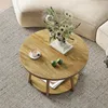 A round coffee table with a floral arrangement, a cup of coffee, and two green fruits on top, placed on a rug next to a sofa. Produktbild-Vorschau