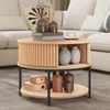 A round coffee table with storage is placed in a living room setting next to a sofa. Produktbild-Vorschau
