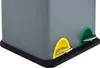A close-up view of the bottom corner of a gray dual-compartment trash can with yellow and green pedal-operated lids. Produktbild-Vorschau