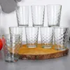 A set of eight clear glasses with a textured pattern, arranged on a wooden slice. Náhled obrázku produktu