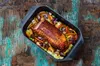 A roasted meat dish with vegetables in a roasting pan, placed on a rustic wooden surface. Náhľad obrázku produktu