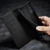 A hand is holding a black phone case over an open black wallet case. Produktbild-Vorschau