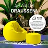 A yellow beanbag chair and ottoman are placed on a patterned rug in a lush, tropical setting with large green plants. Anteprima dell’immagine prodotto