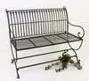 A dark metal garden bench with decorative scrollwork on a white background, with a small potted plant and ivy at its base. Produktbild-Vorschau