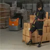 A man in a warehouse is using a scanner to scan a box, with a forklift and stacks of boxes in the background. Produktbild-Vorschau