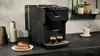 A black Siemens espresso machine is shown on a kitchen counter, with two eclairs on a plate in the foreground and a cup of coffee on a saucer in the background. Náhled obrázku produktu