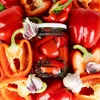 A close-up overhead view of red bell peppers, garlic, and a glass jar filled with pickled red peppers and peppercorns. Produktbild-Vorschau