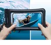 Hands holding a waterproof phone case with a surfer visible on the phone screen, set against a blue water background. Podgląd zdjęcia produktu