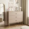 A dresser with three drawers is placed in a room with artwork on the wall and a large mirror. Náhled obrázku produktu