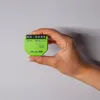 A hand holding a small green electronic device against a light gray background. Produktbild-Vorschau